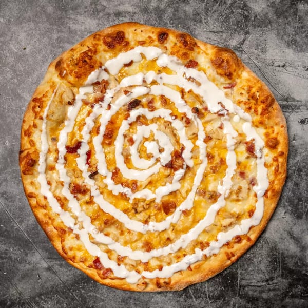 Overhead view of a round pizza with melted cheese, bacon, and a spiral of white sauce.