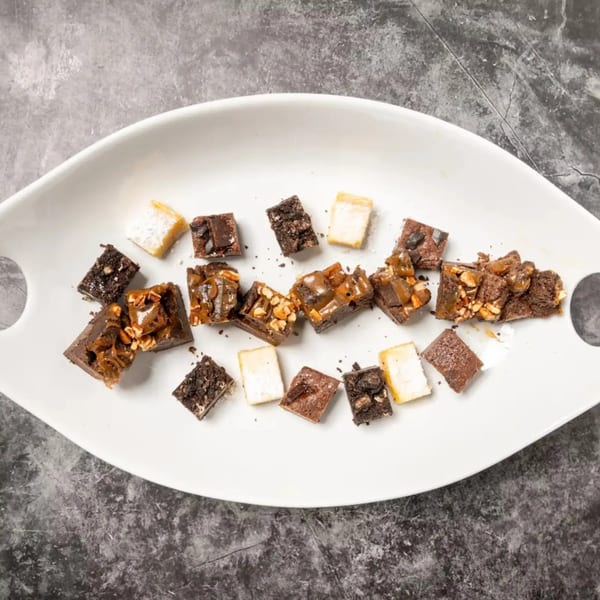 Assortment of brownies and blondies with various toppings on a white platter.
