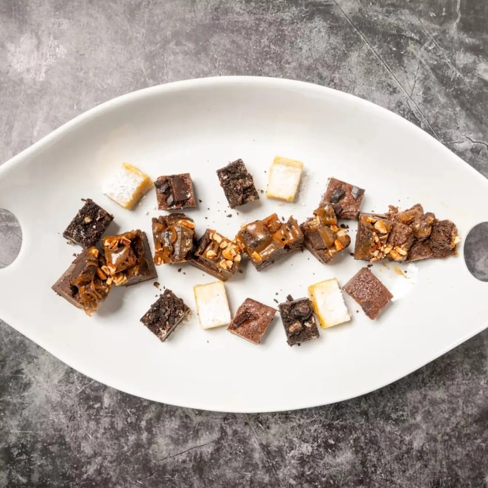 Assortment of brownies and blondies with various toppings on a white platter.