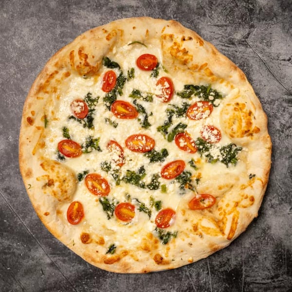 White pizza with melted cheese, spinach, halved cherry tomatoes, and crumbled feta on a dark surface.