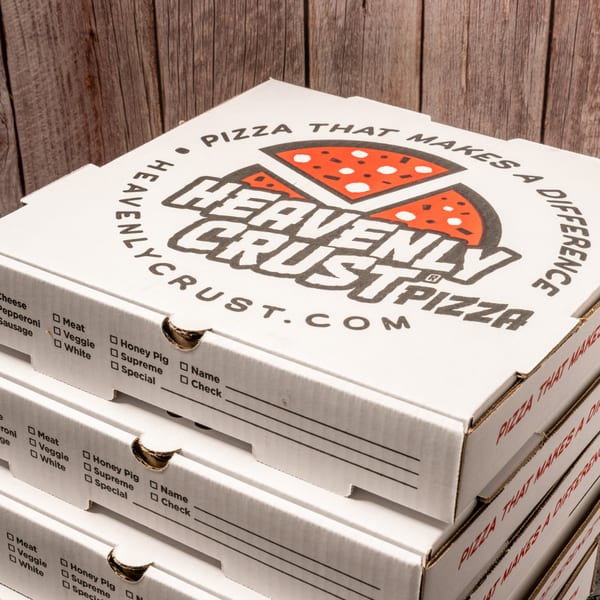 Stack of Heavenly Crust Pizza boxes with a wooden background.