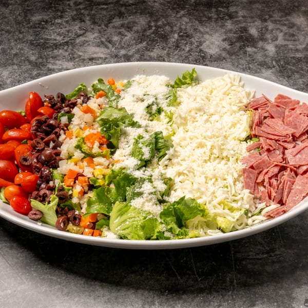 A large white oval bowl filled with a colorful salad on a dark gray surface.