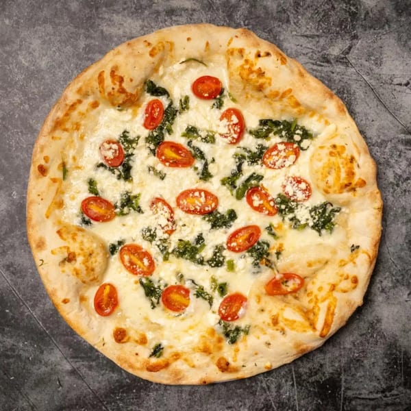 White pizza with spinach, cherry tomatoes, and feta cheese on a dark gray surface.