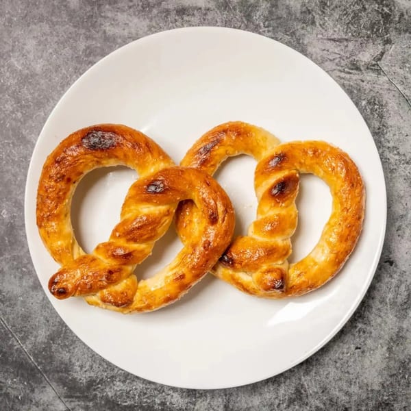A golden-brown, twisted pretzel with a slightly burnt top, served on a white plate.